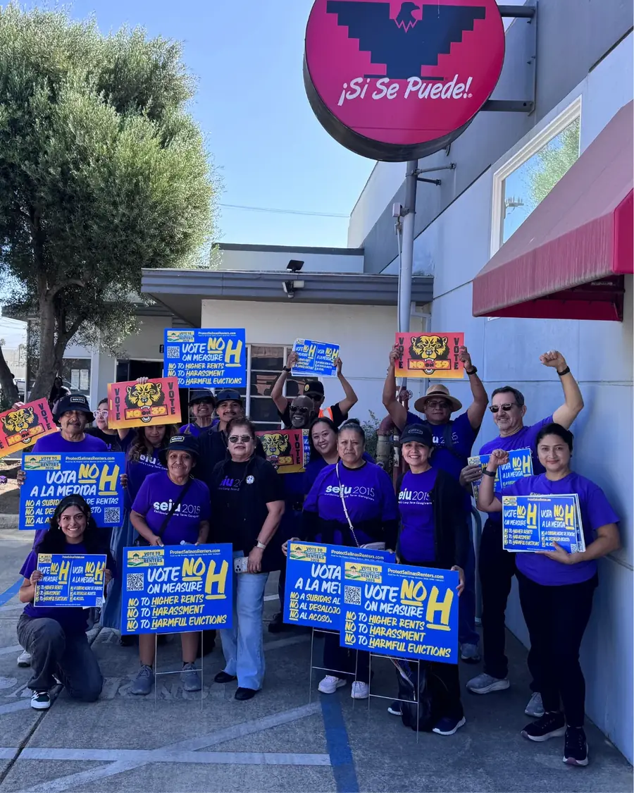 Volunteers in purple SEIU 2015 shirts hold Vote NO on Measure H yard signs, in English and Spanish.